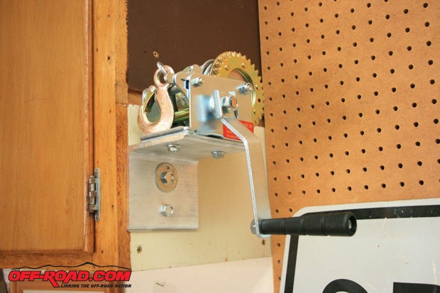Since my adjacent garage wall surface is covered with a permanently mounted pegboard, I picked a cabinet sidewall for the brake winch bracket. I had to reinforce the cabinets attachment in order to be assured that the cabinet would hold the top in place indefinitely.