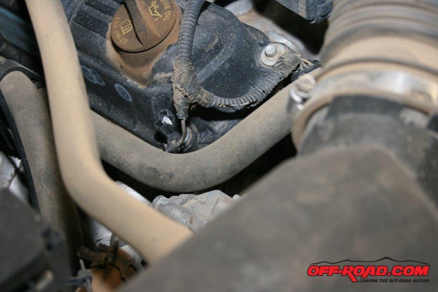 The factory switch location is below these hoses on the passenger-side front corner of the V6, behind the band tensioner. Its hard to find, tough to see, and even harder to remove. It also requires a special tool called an oil pressure switch socket to remove the OEM switch.
